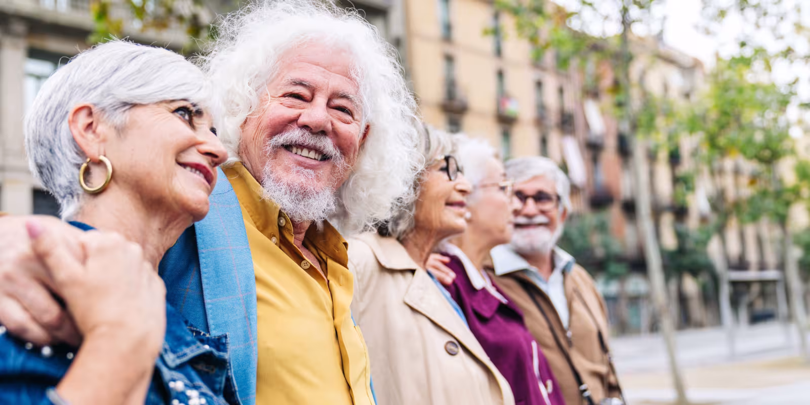 A group of retirees stand in a line posing for a picture on a sightseeing trip in a city. 