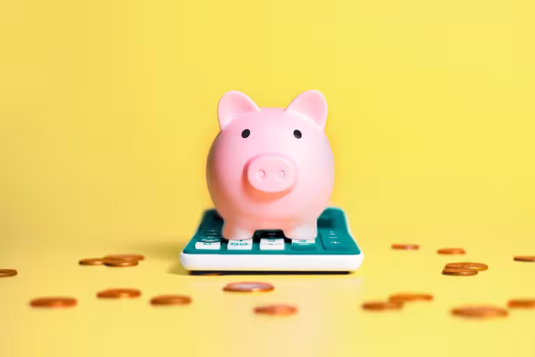 A piggy bank sits on top of a calculator with pennies strewn across the space around it. 