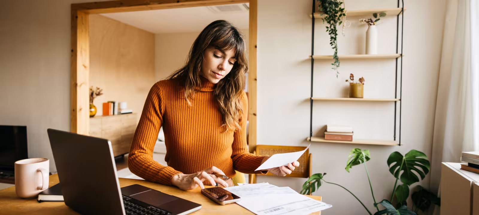 A woman sits at her desk reviewing paperwork and calculating a bill. 