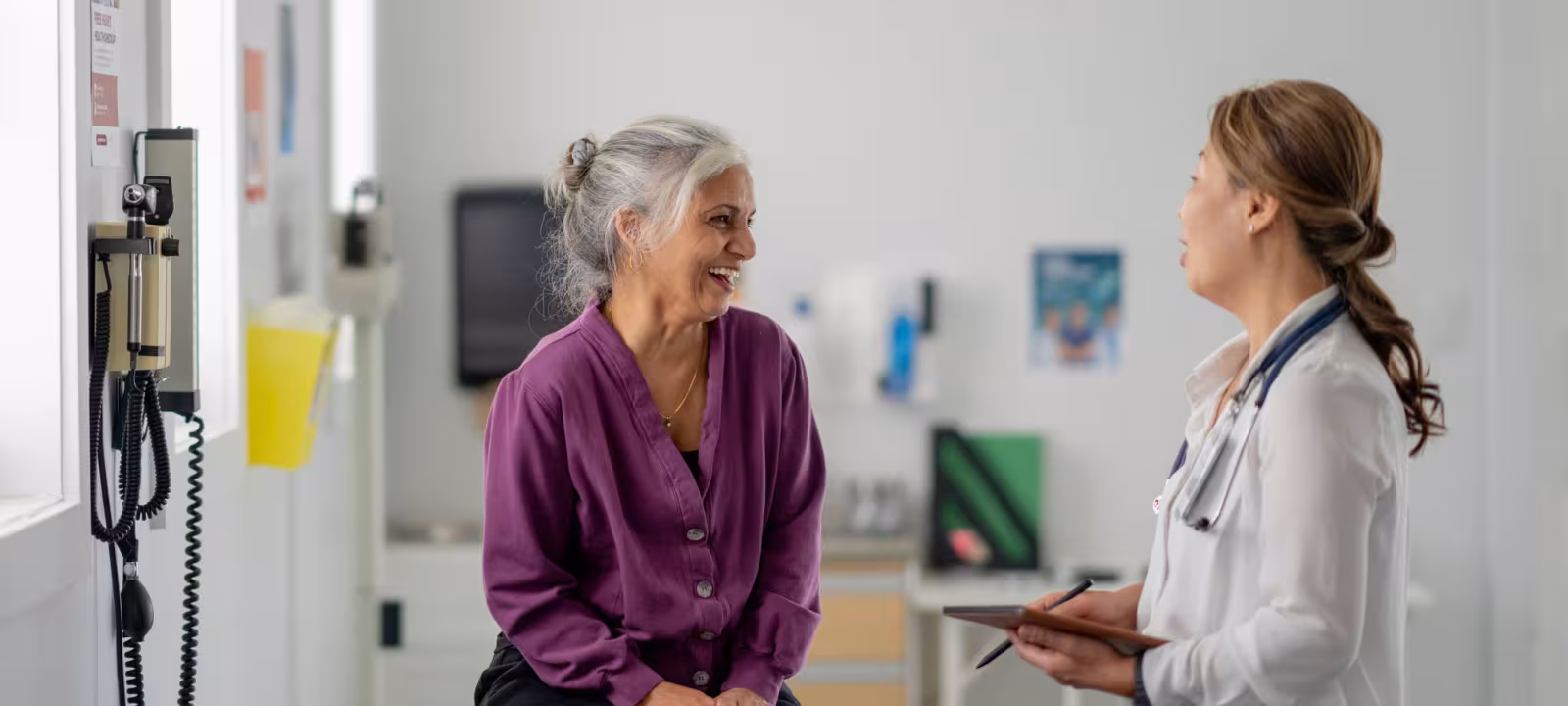 An older woman sits on an exam bench while speaking with her doctor
