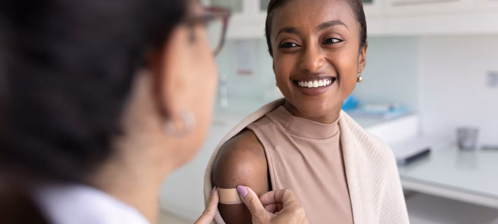 A woman smiles while a doctor puts a bandage on her arm over a vaccination site