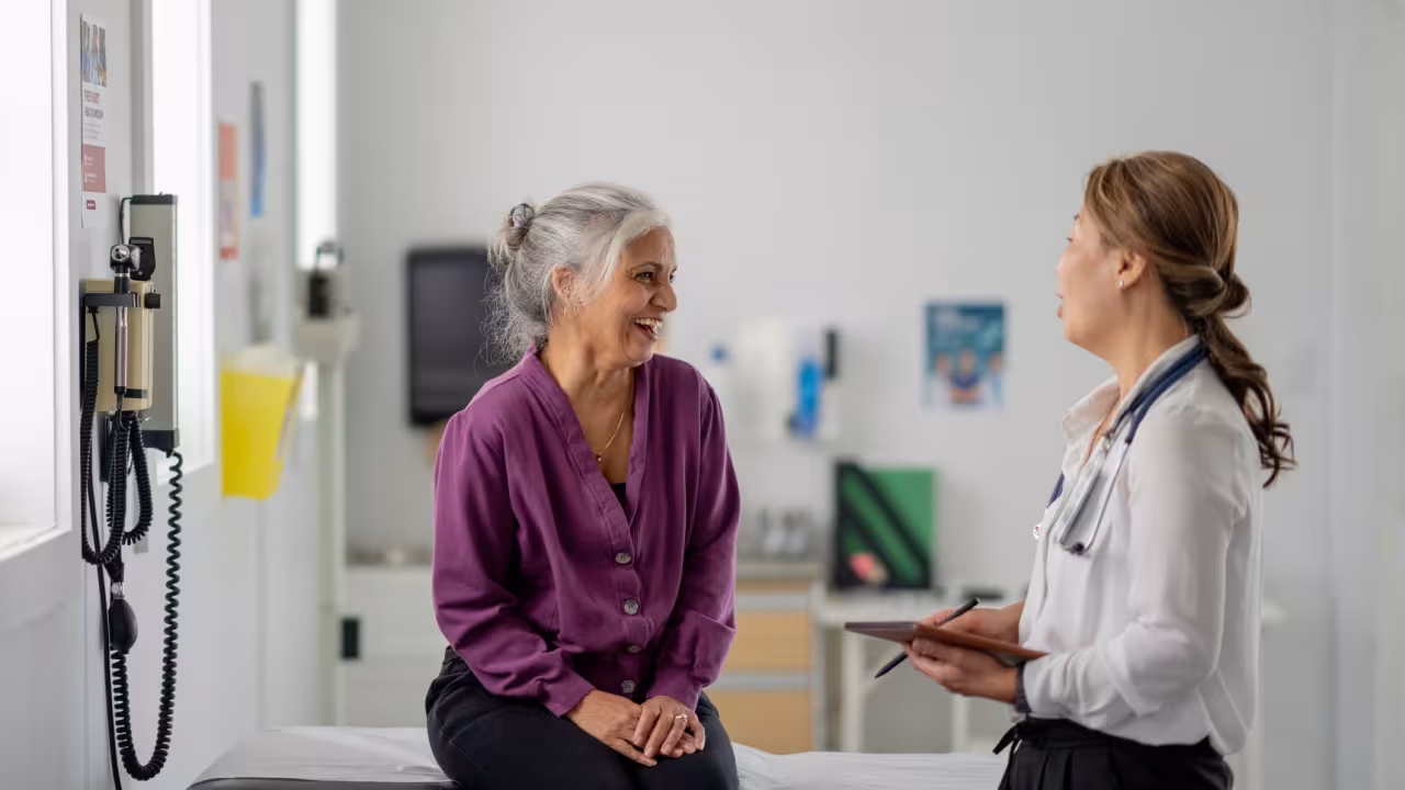 An older woman sits on an exam bench while speaking with her doctor