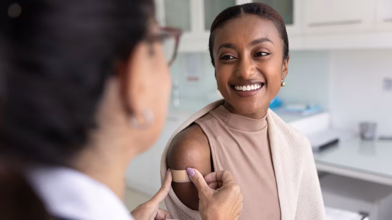 A woman smiles while a doctor puts a bandage on her arm over a vaccination site